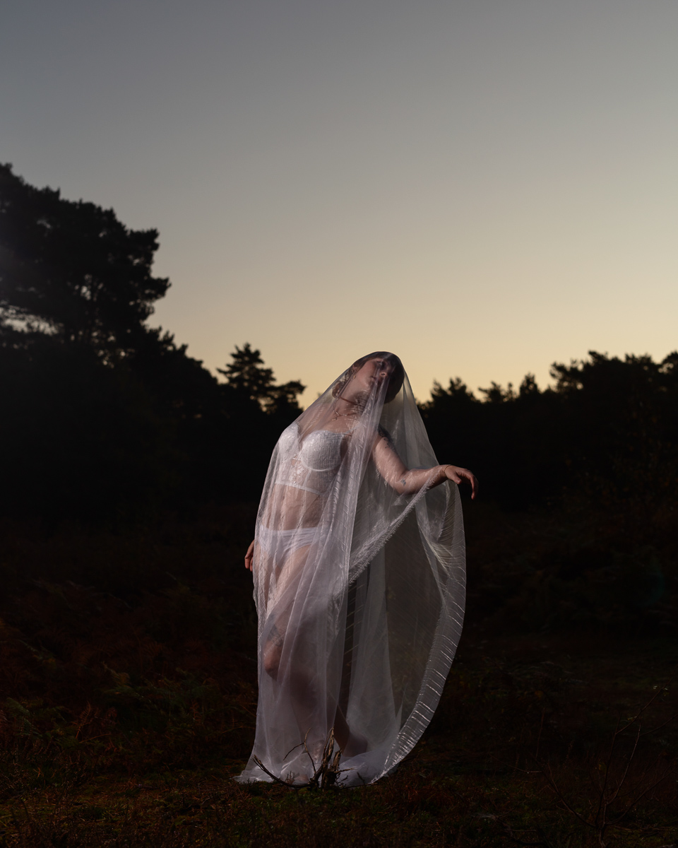 Person draped in translucent white fabric in forest at dusk