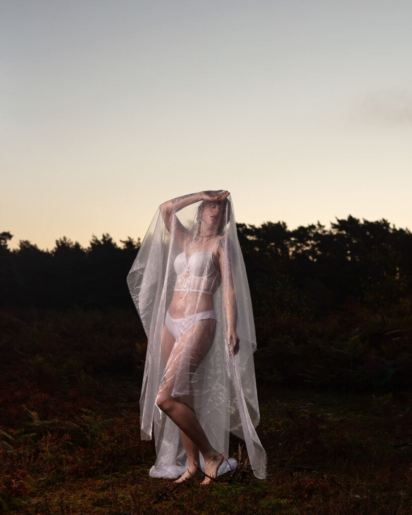 Woman in white sheer fabric posing at sunset in countryside