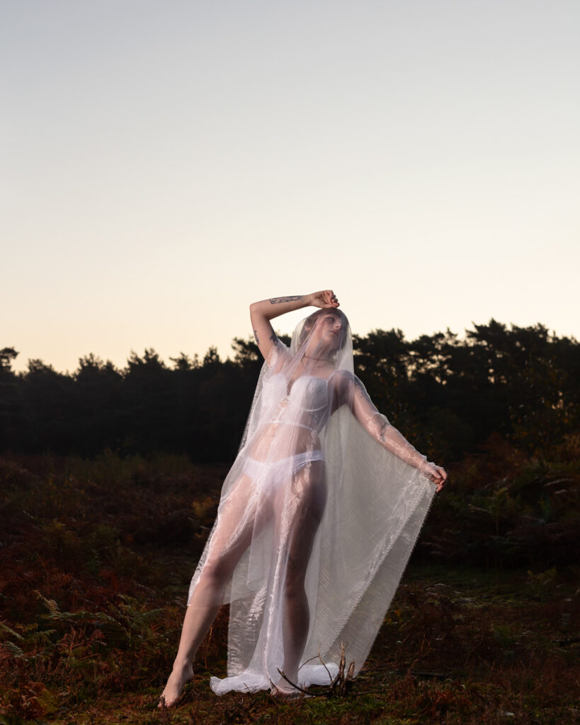 Woman in flowing white veil posing in countryside field at dusk