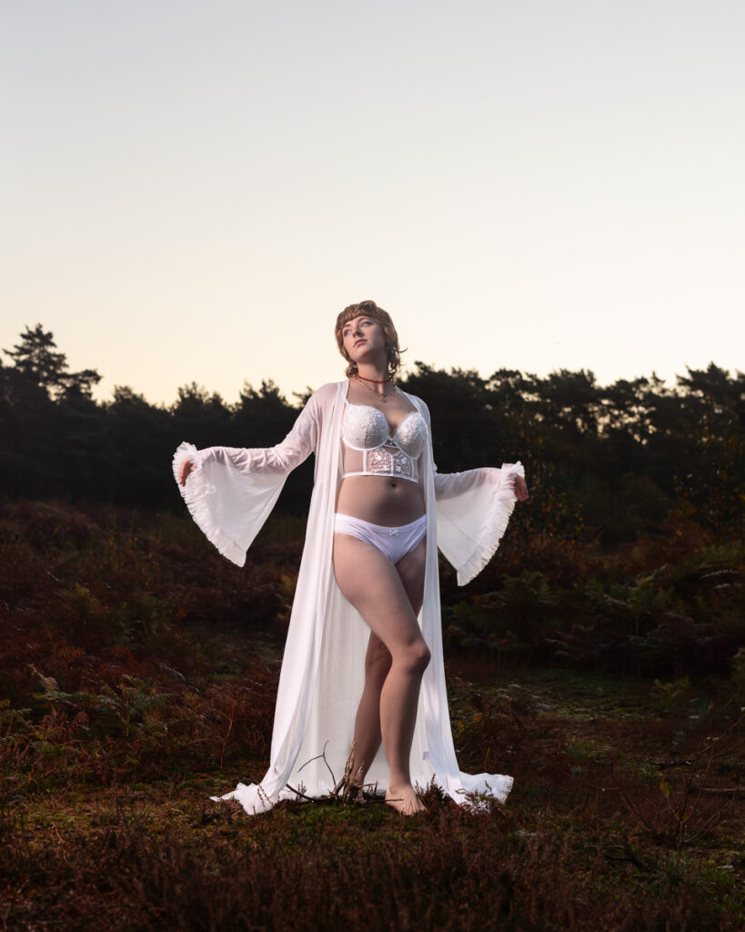 Woman in white lingerie and flowing robe in countryside landscape