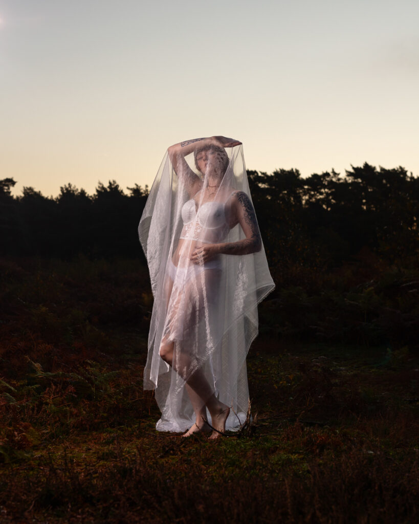 Woman in white dress and veil standing in rural field at dusk