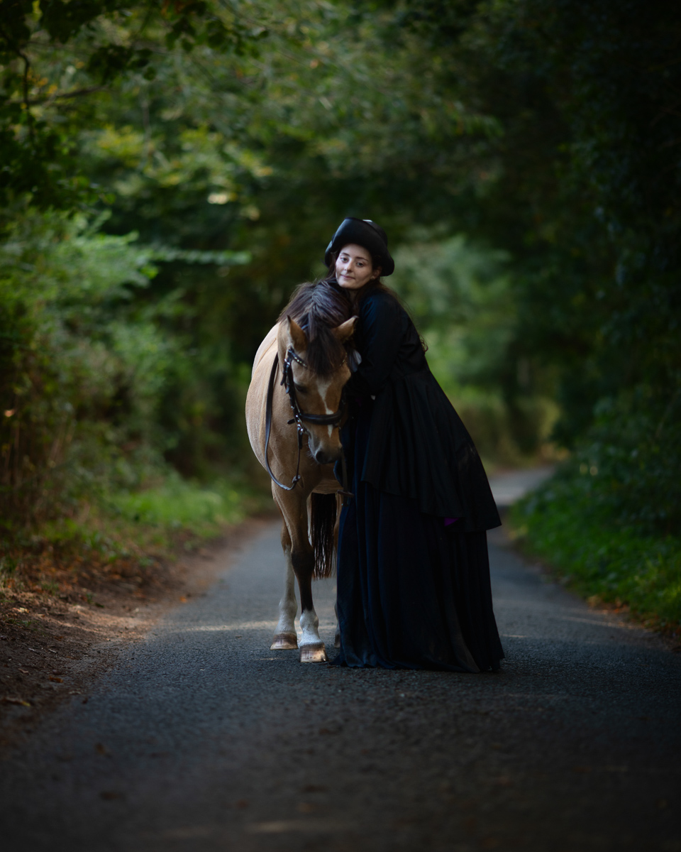 Woman in black cloak with horse on forest path