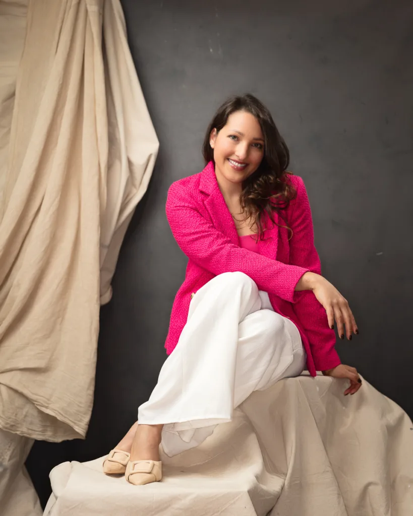 Woman in pink blazer and white trousers sitting smiling