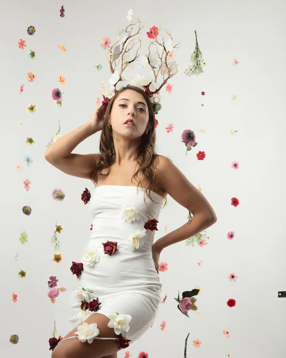 Woman in white dress wearing floral branch headpiece surrounded by flowers
