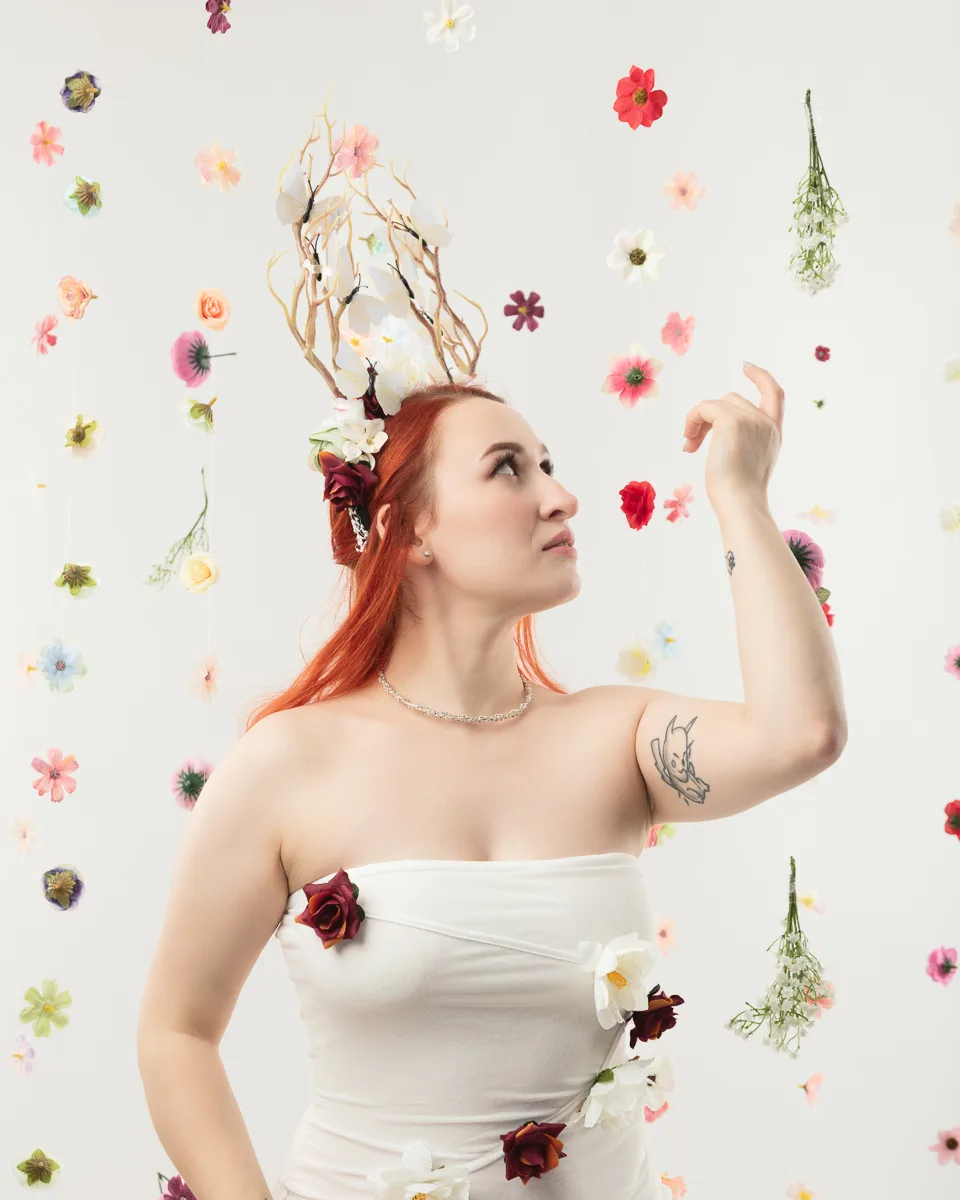 Woman with red hair wearing floral crown surrounded by flowers
