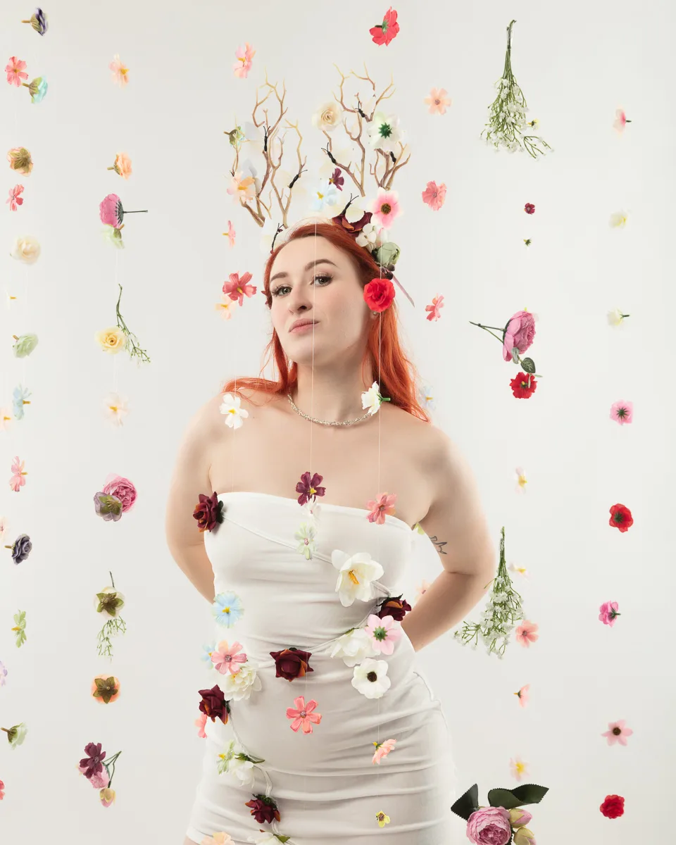 Woman with red hair wearing white dress surrounded by flowers