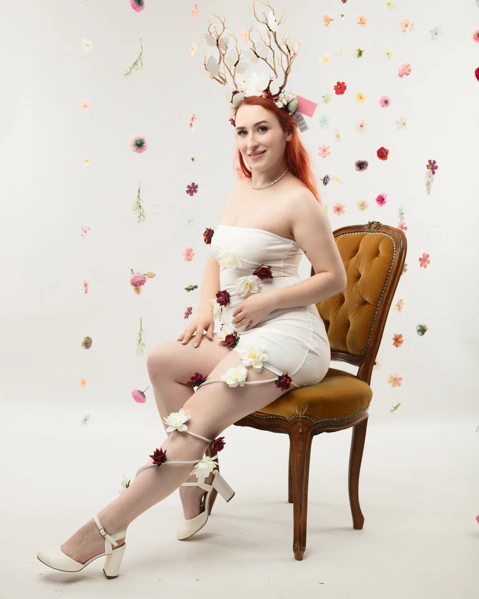 Woman with red hair wearing antler headpiece and white dress sitting on chair