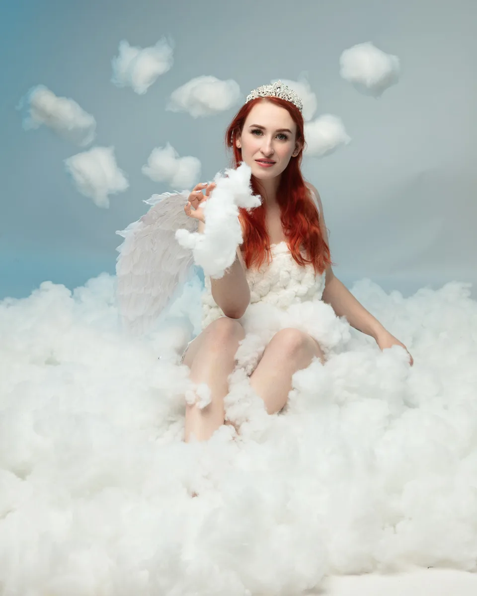 Woman with red hair wearing tiara and white wings sitting on clouds