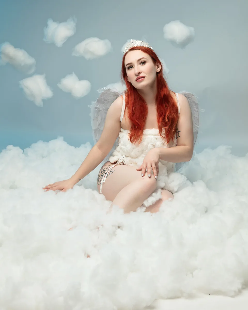 Woman with red hair wearing angel wings sitting on clouds