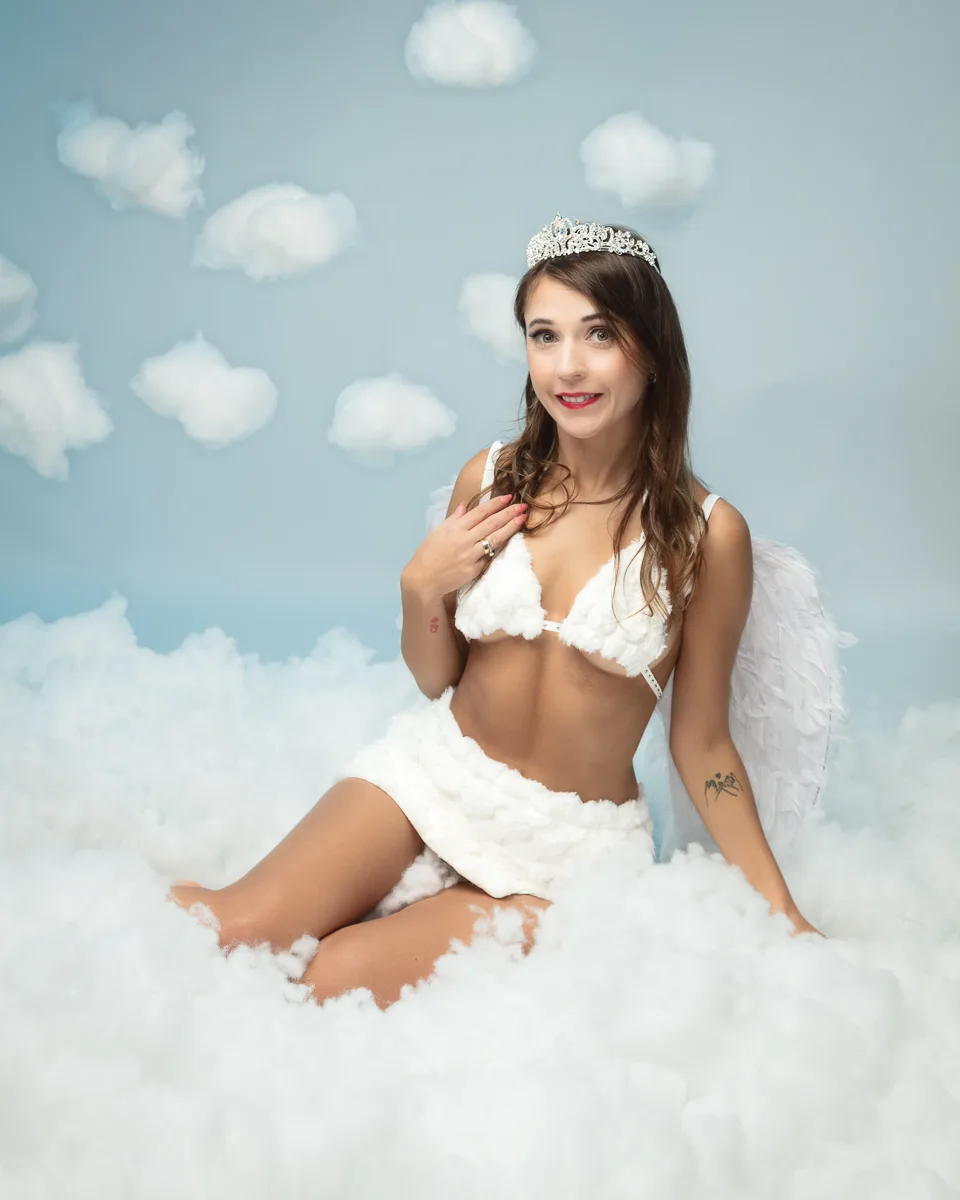 Woman wearing tiara and angel wings sitting on clouds