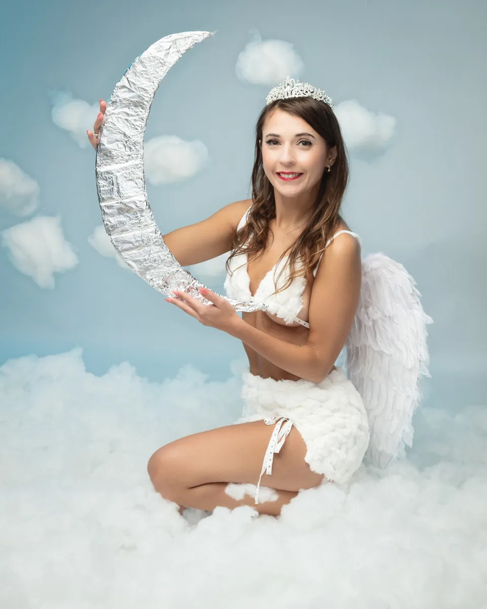 Woman dressed as angel holding silver crescent moon prop