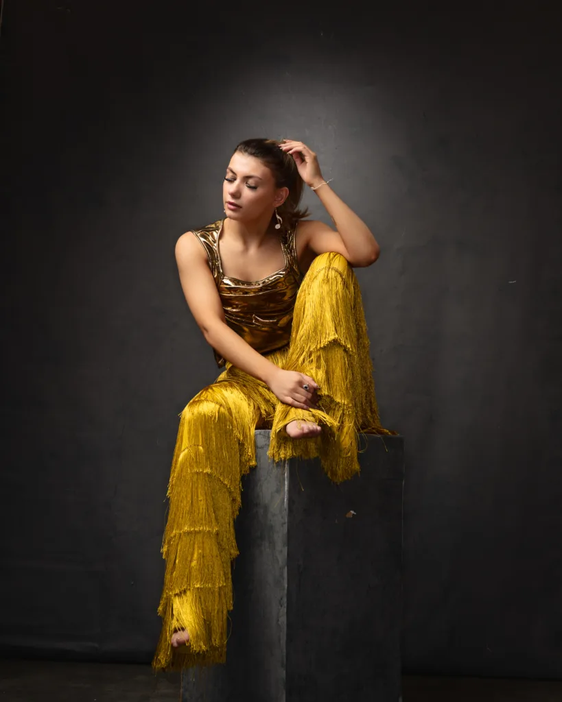 Woman in golden outfit sitting pose.