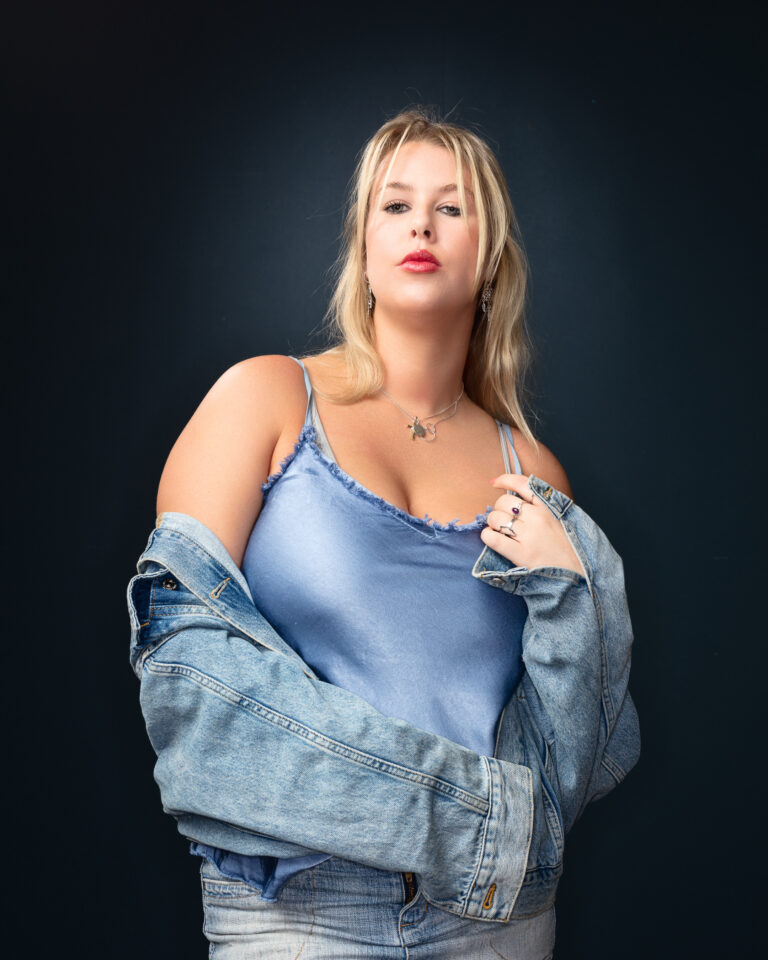 Woman in denim jacket, blue top posing confidently.