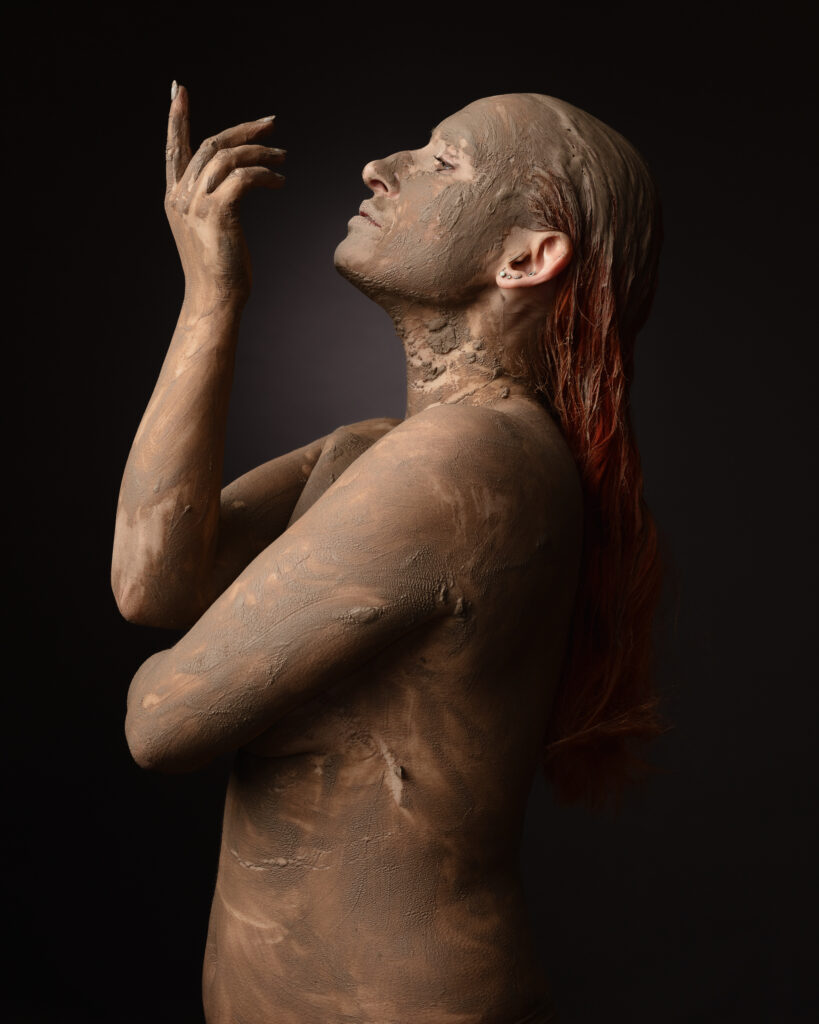 Person covered in mud posing artistically.