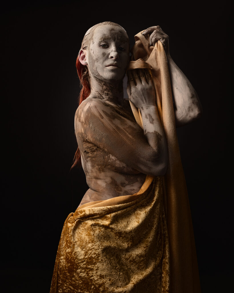 Person covered in clay holding a golden cloth.
