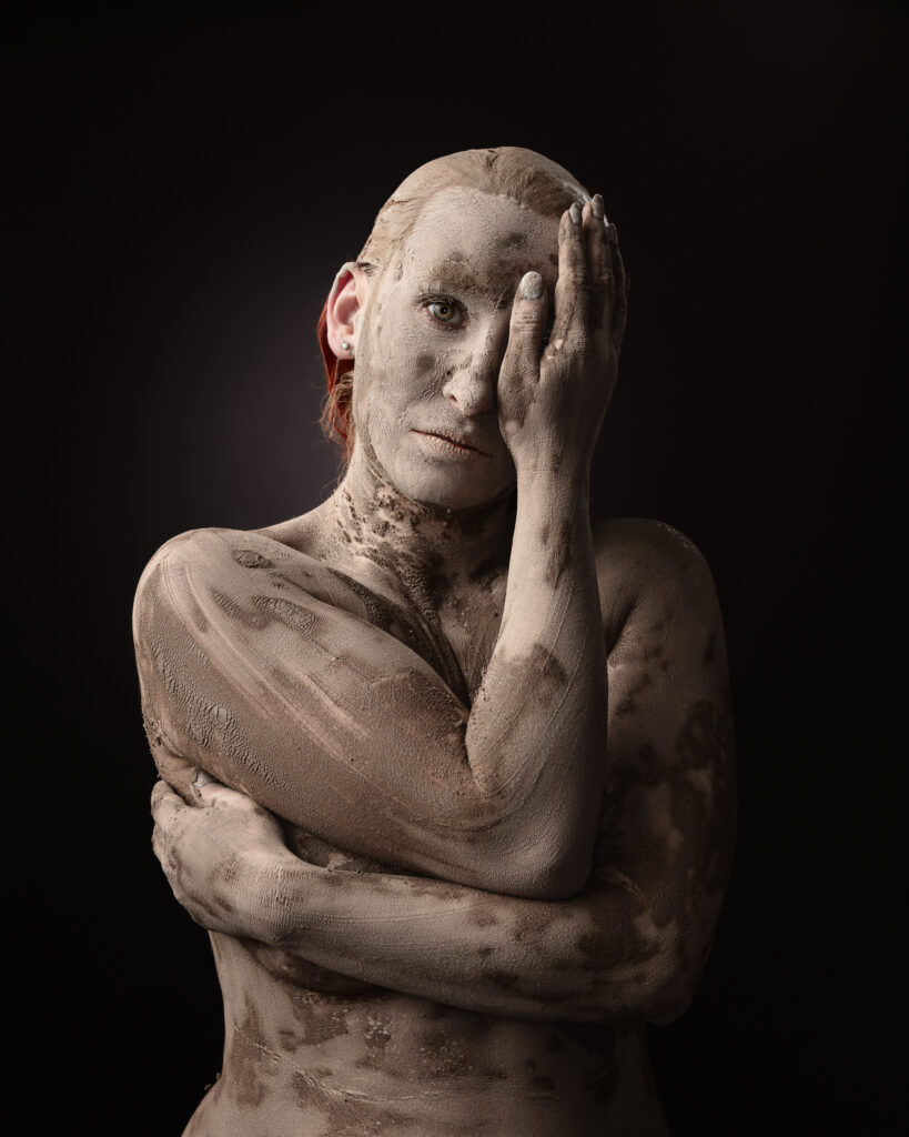Person covered in mud, holding their face.