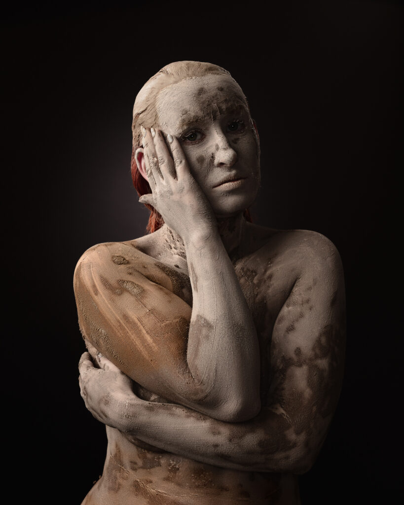 Person covered in clay against dark background.