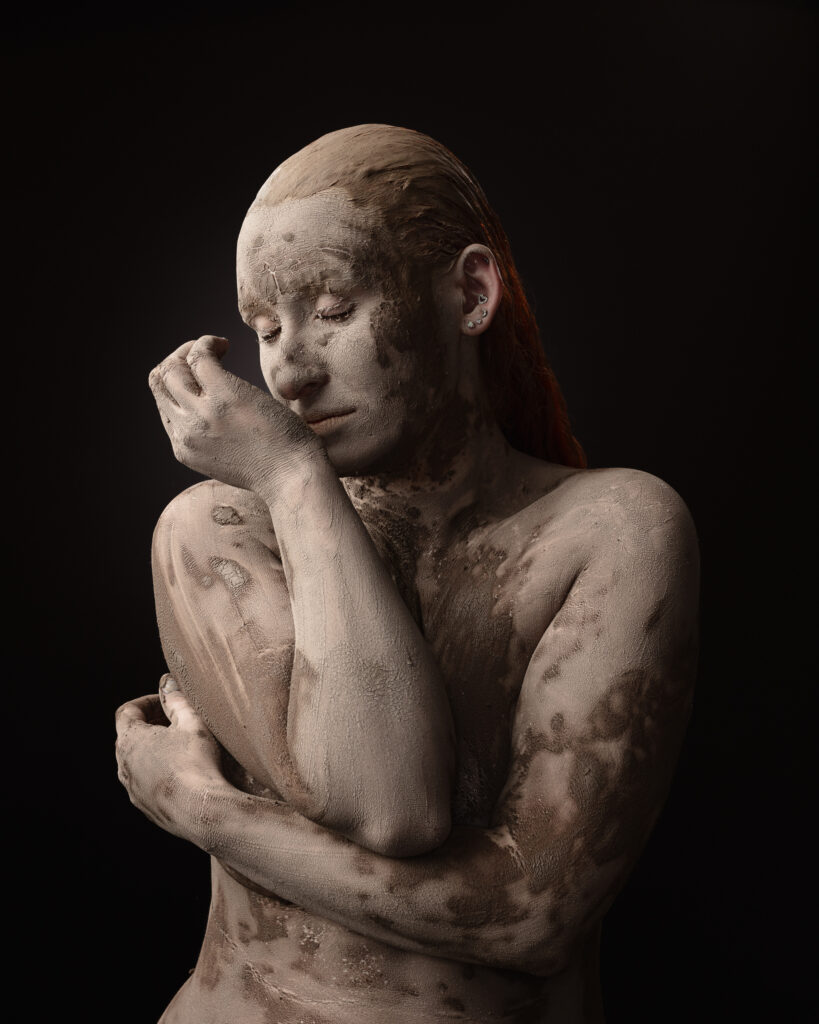 Person covered in clay against dark background.