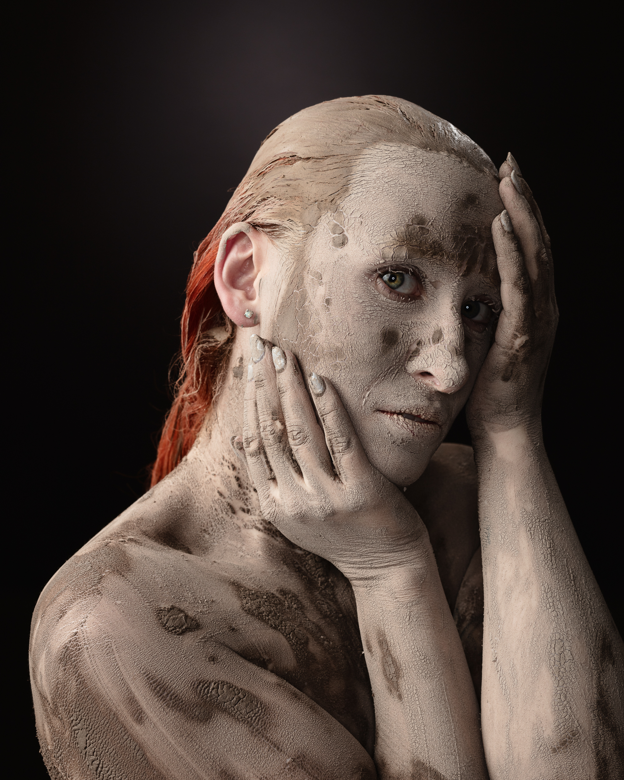 Person covered in mud against dark background
