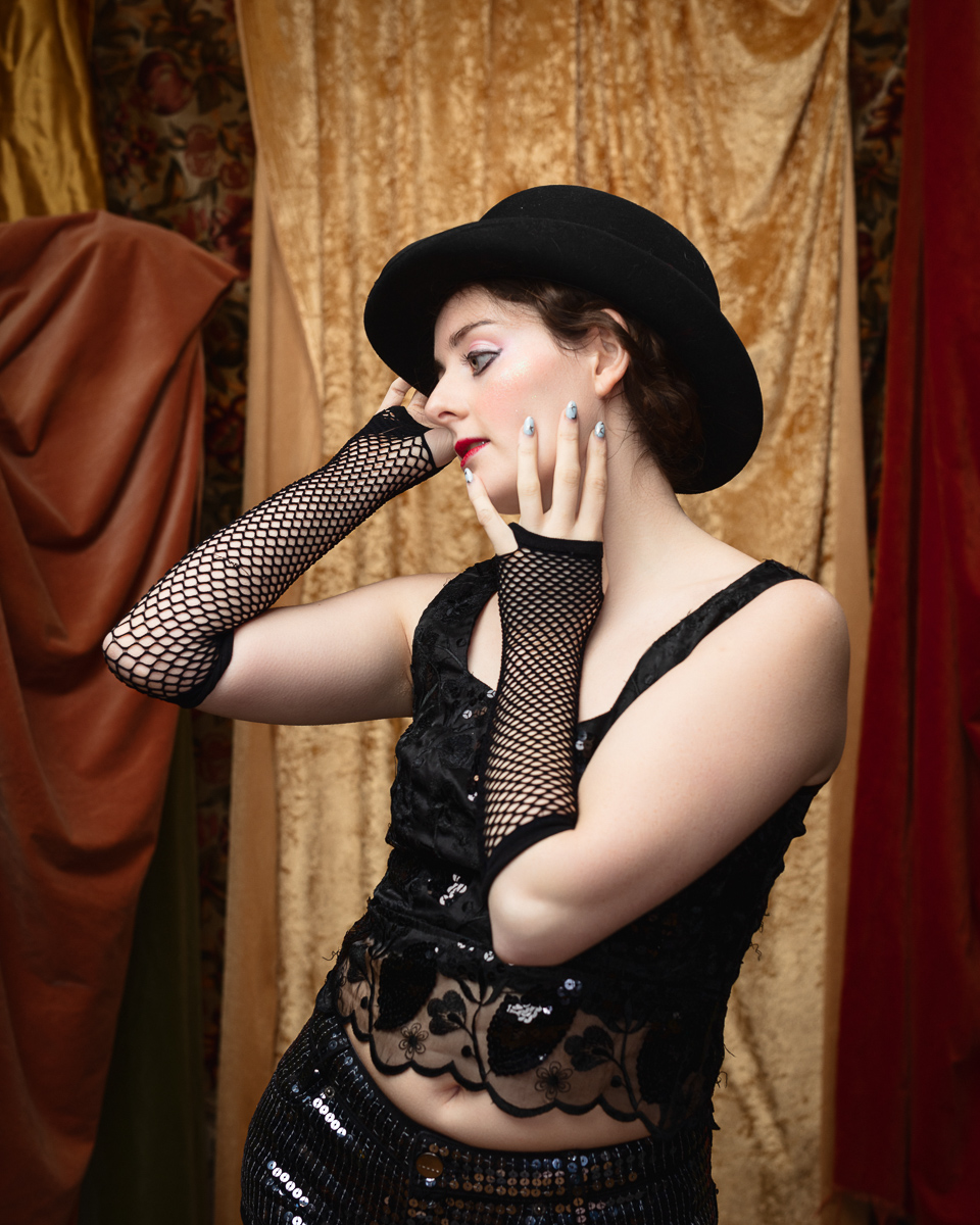 Woman in black hat and fishnet gloves posing.