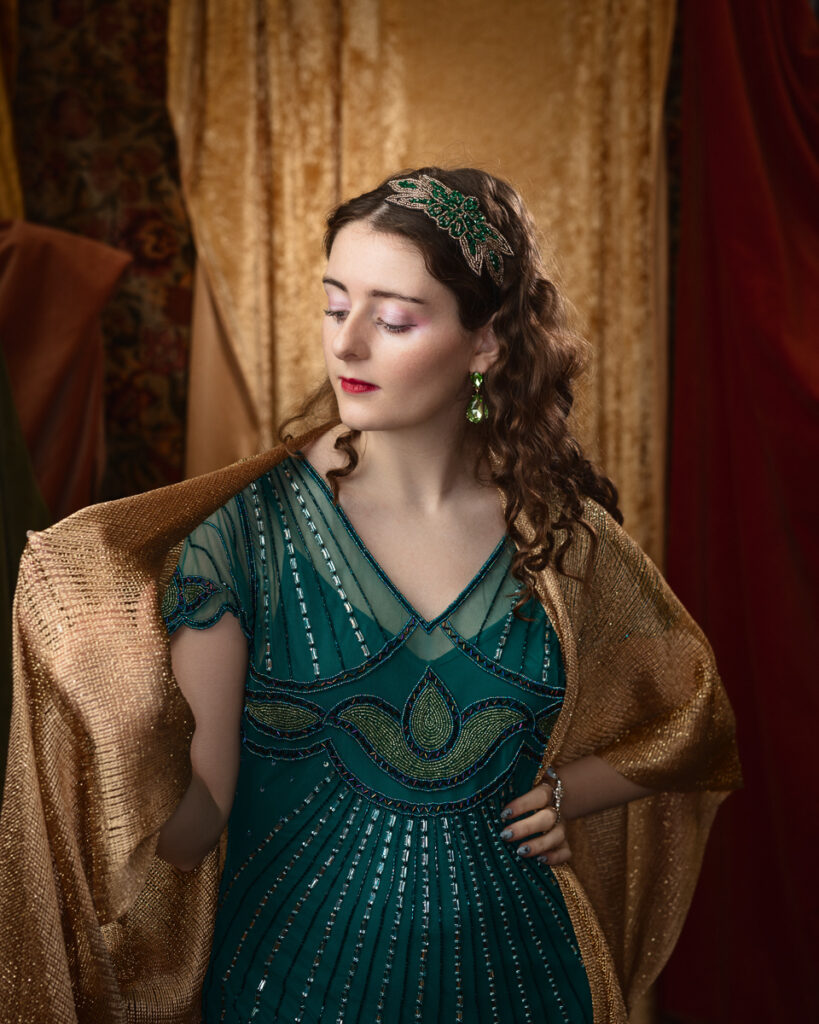 Woman in vintage green dress, gold shawl, floral hairpiece.