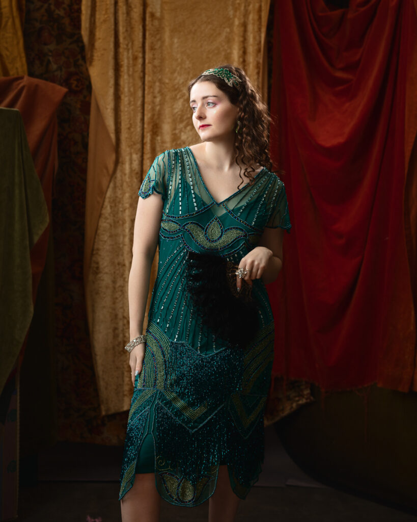 Woman in green vintage dress holding fan.