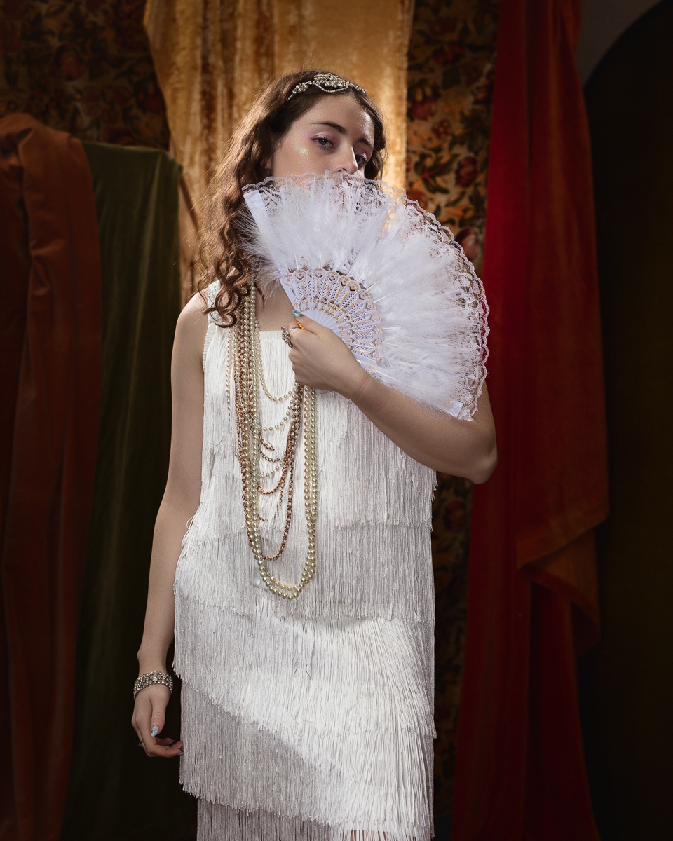 Woman in vintage dress holding ornate fan.