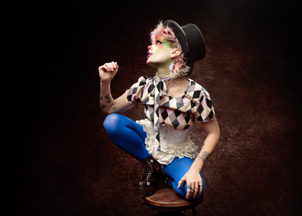 Person in colourful outfit posing artistically on stool.