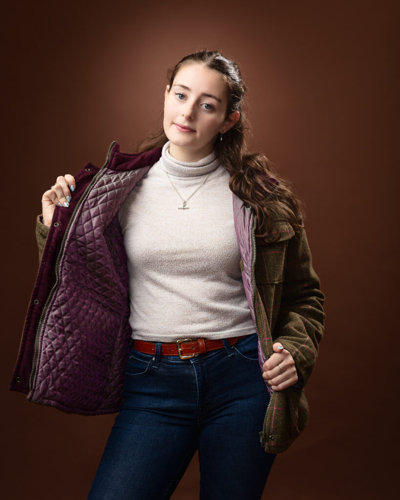 Person in a jacket and turtleneck against brown background.