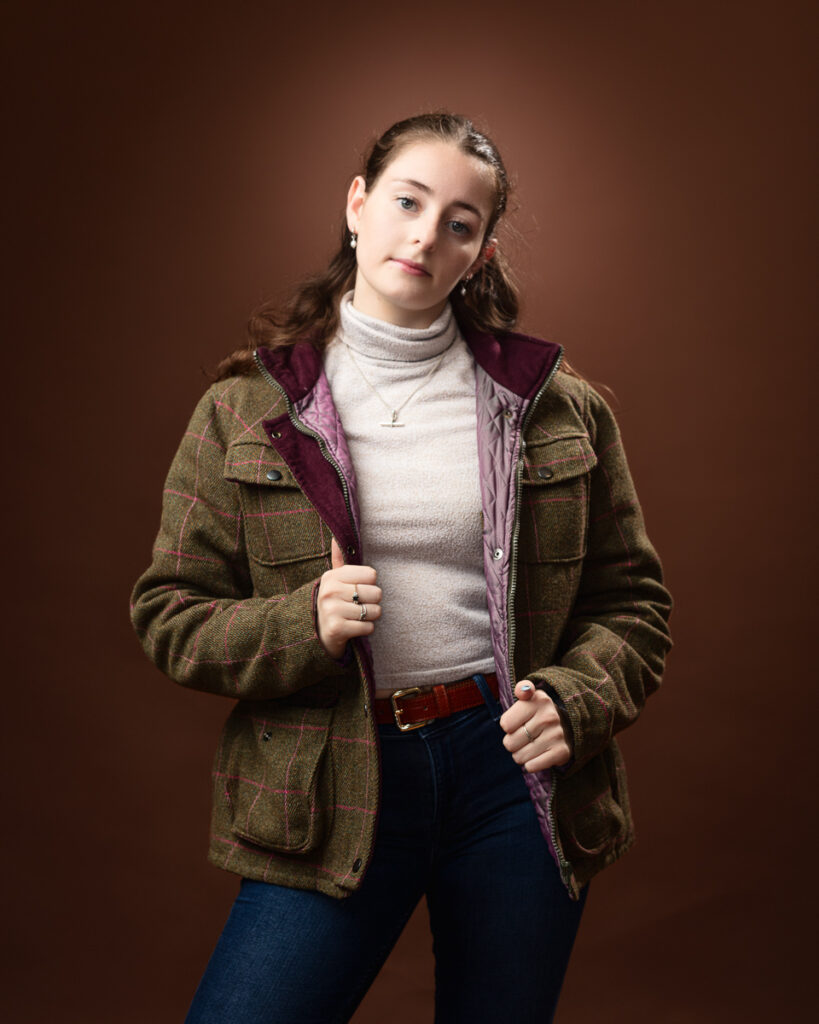 Woman in jacket posing against brown background.