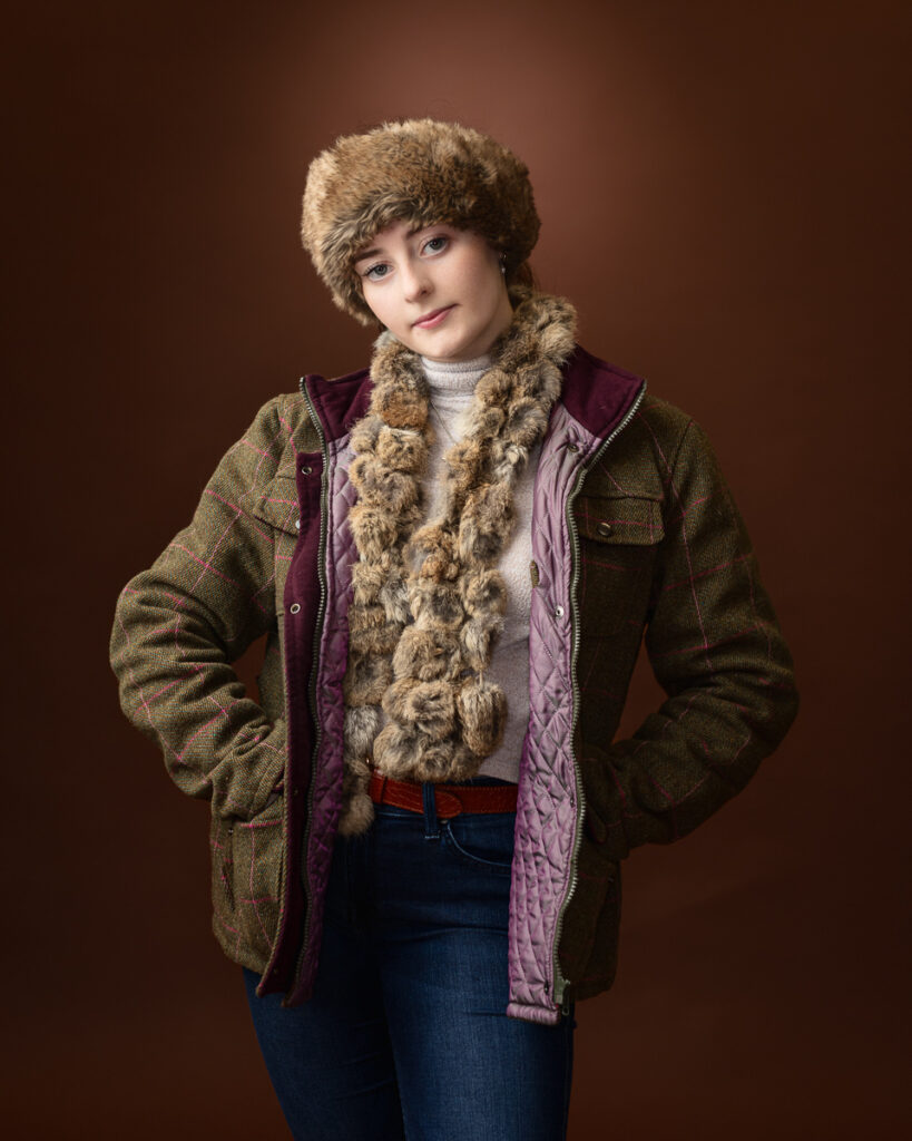 Country-style studio portrait of Sophia in a tweed jacket, fur hat and scarf, hands in pockets