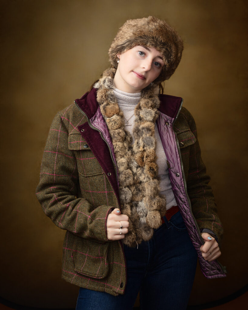 Country-style studio portrait of Sophia in a tweed jacket, fur hat and scarf, gentle smile