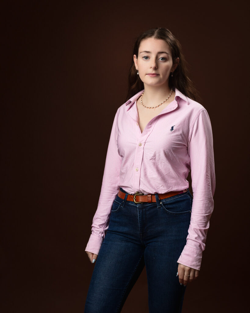 Studio portrait of Sophia in a pink striped shirt and jeans, direct gaze