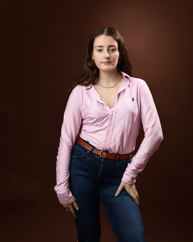 Studio portrait of Sophia in a pink striped shirt and jeans, hands at her waist
