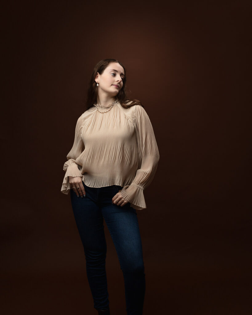 Studio portrait of Sophia in a cream pleated blouse and jeans, walking pose looking to the side