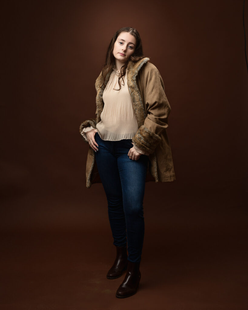 Person in coat, standing against brown backdrop.