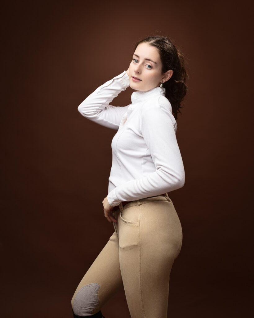 Equestrian-style studio portrait of Sophia in a white riding top and tan jodhpurs, side profile
