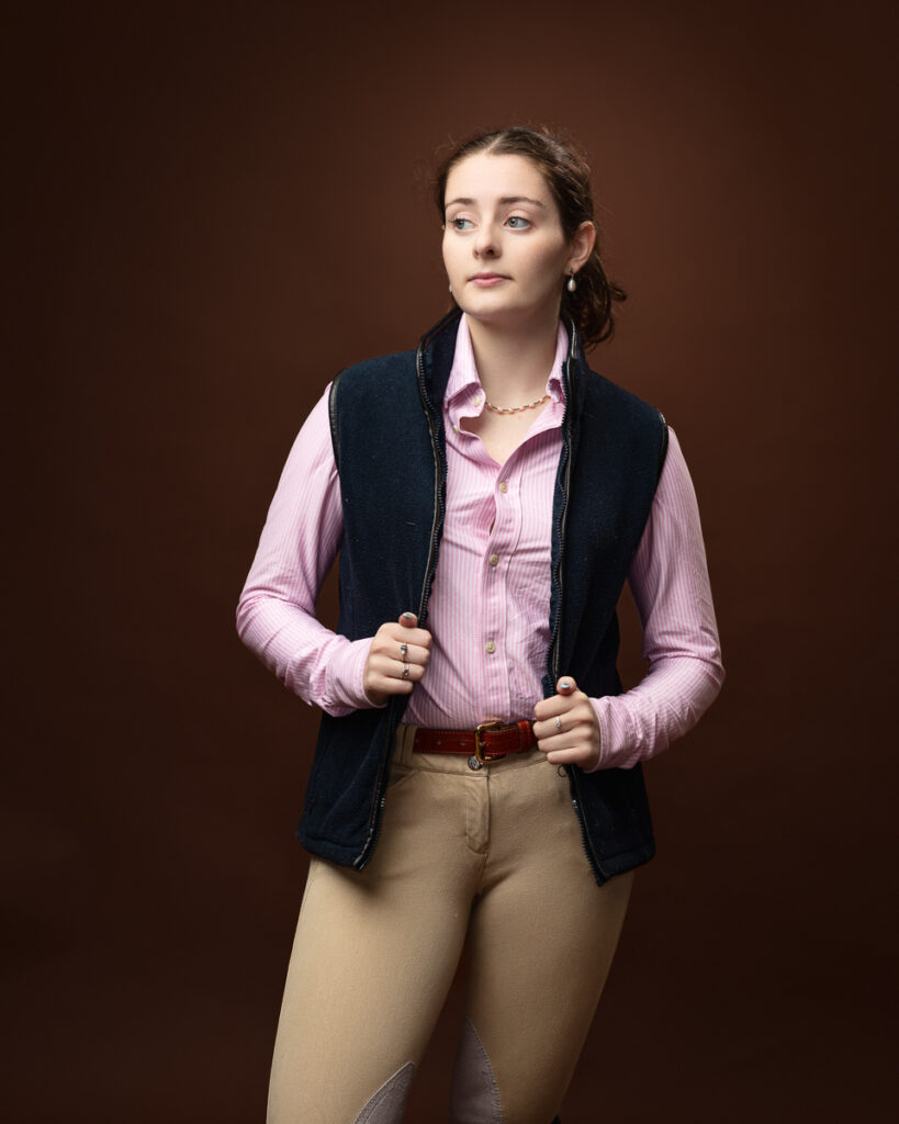 Equestrian-style studio portrait of Sophia in a navy gilet over a pink shirt, hands on the lapels