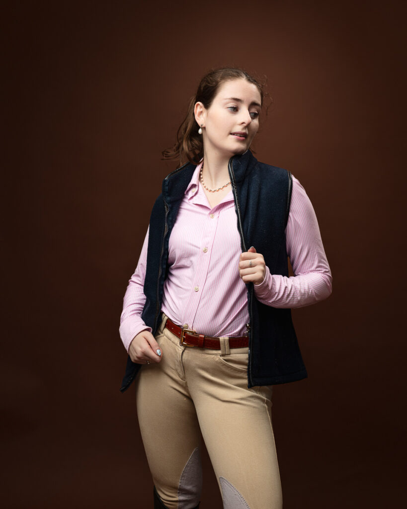 Equestrian-style studio portrait of Sophia in a navy gilet over a pink shirt, looking to the side