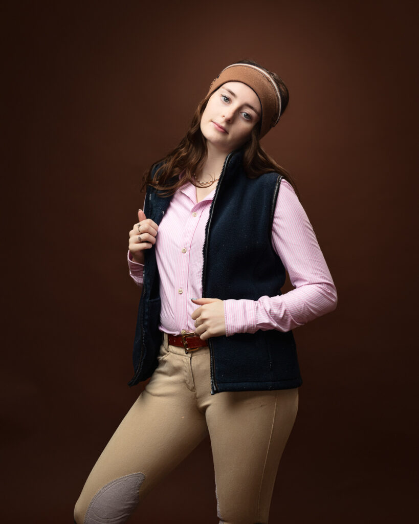 Equestrian-style studio portrait of Sophia in a navy gilet over a pink shirt with a headband, holding the lapel