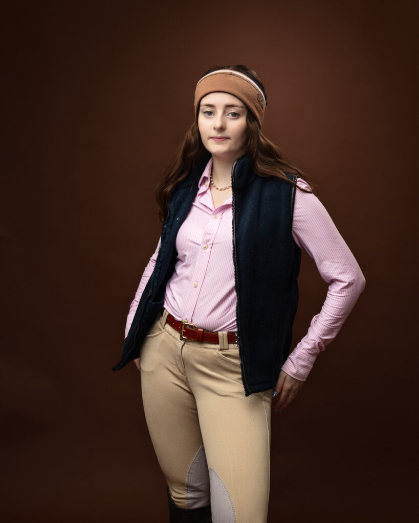 Equestrian-style studio portrait of Sophia in a navy gilet over a pink shirt with a headband, direct gaze