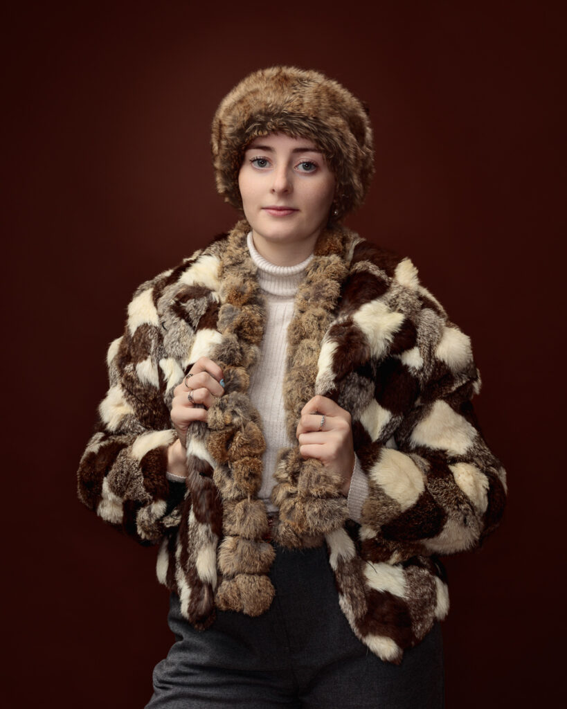 Close studio portrait of Sophia in a patchwork faux fur coat and matching fur hat with pom-pom trim