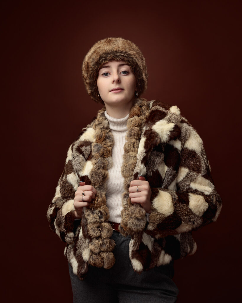 Studio portrait of Sophia in a patchwork faux fur coat and matching fur hat, holding the lapels