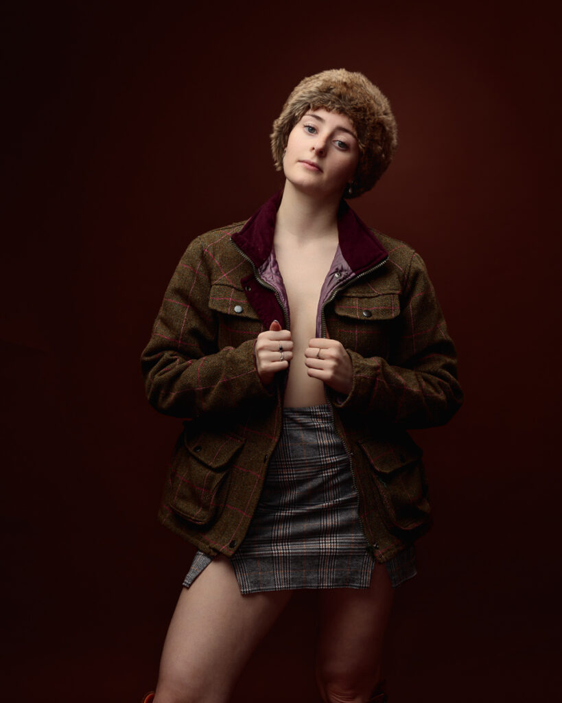 Person in hat and plaid skirt, brown background.