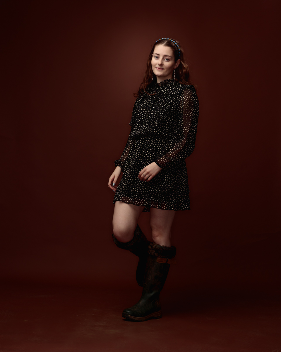 Woman in spotted dress and boots posing confidently.