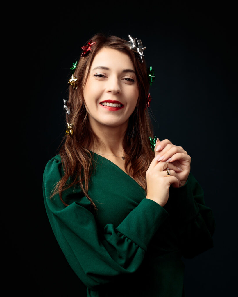 Smiling woman in green dress with festive hair ribbons.
