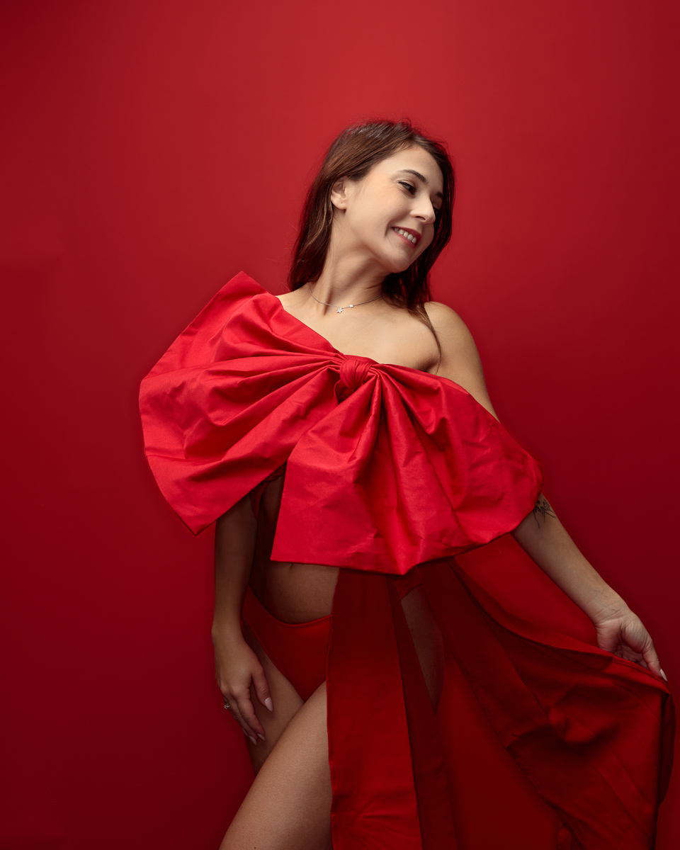 Woman in red dress, smiling against red background.