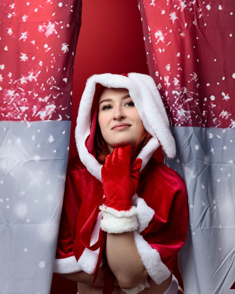 Woman in Santa outfit behind red curtains.