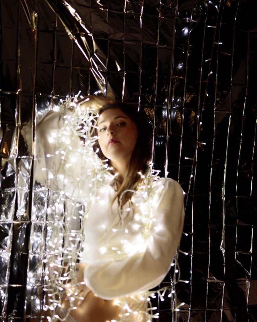 Person wrapped in white fairy lights, reflective backdrop.