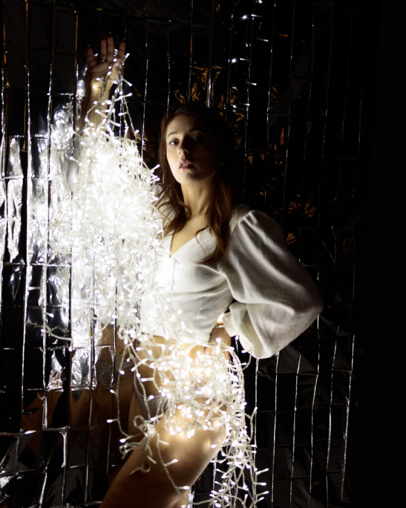 Woman wrapped in fairy lights, mirror background.